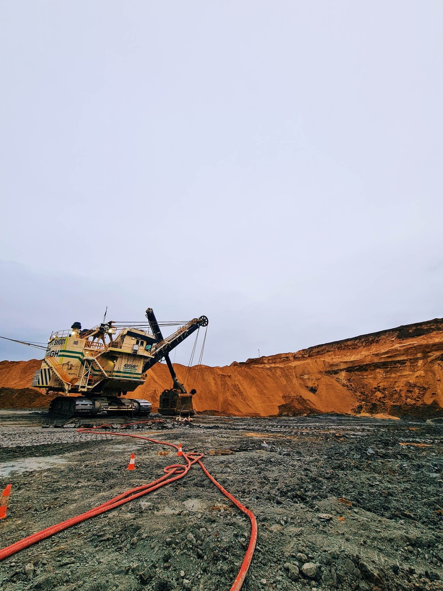 Dragline working a coal strip at dusk with hoses and cones laid out across the bench